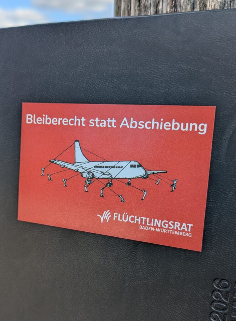 Roter Sticker mit Aufschrift Bleiberecht statt Abschiebung auf schwarzem Grund