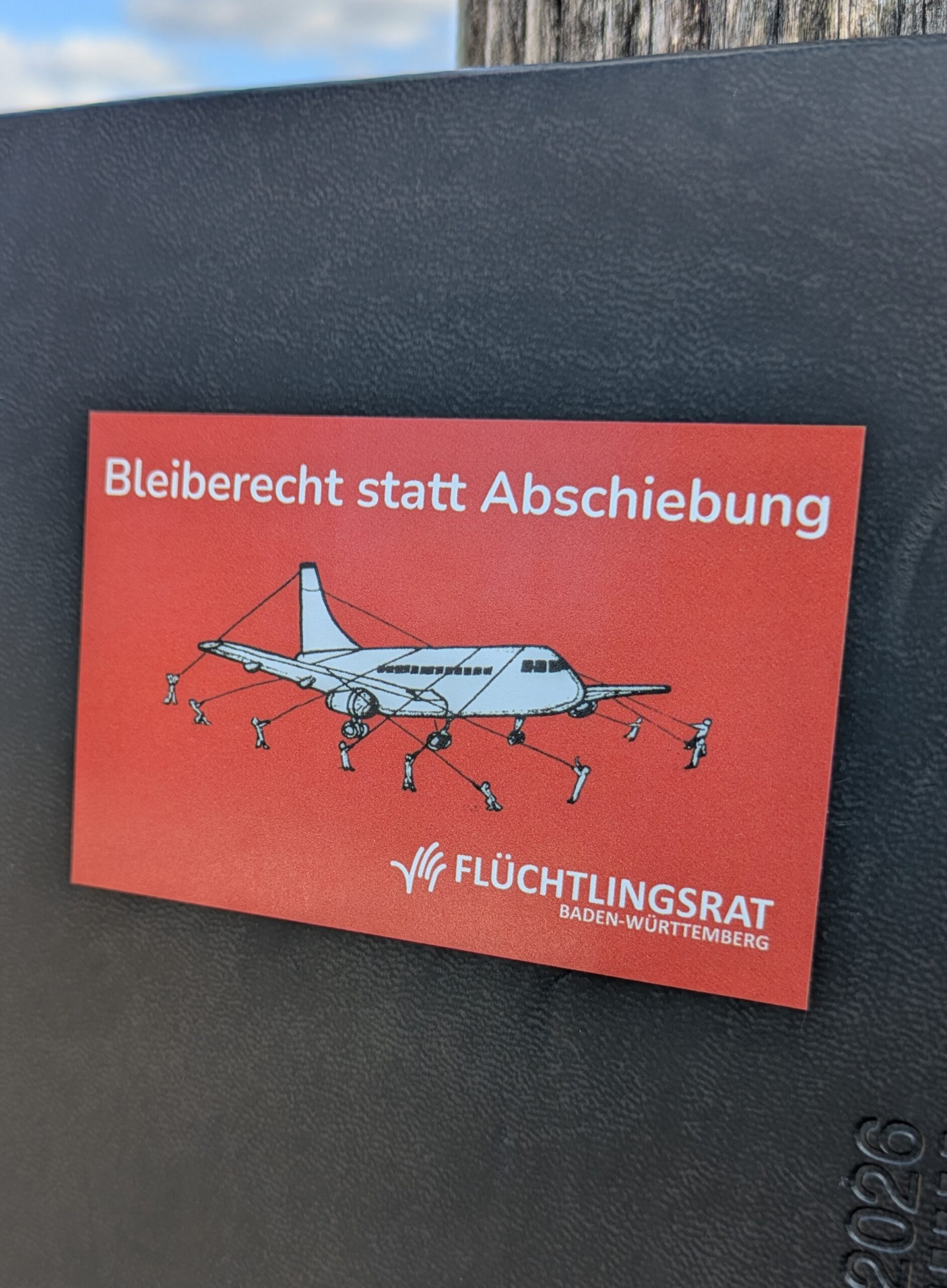 Roter Sticker mit Aufschrift Bleiberecht statt Abschiebung auf schwarzem Grund
